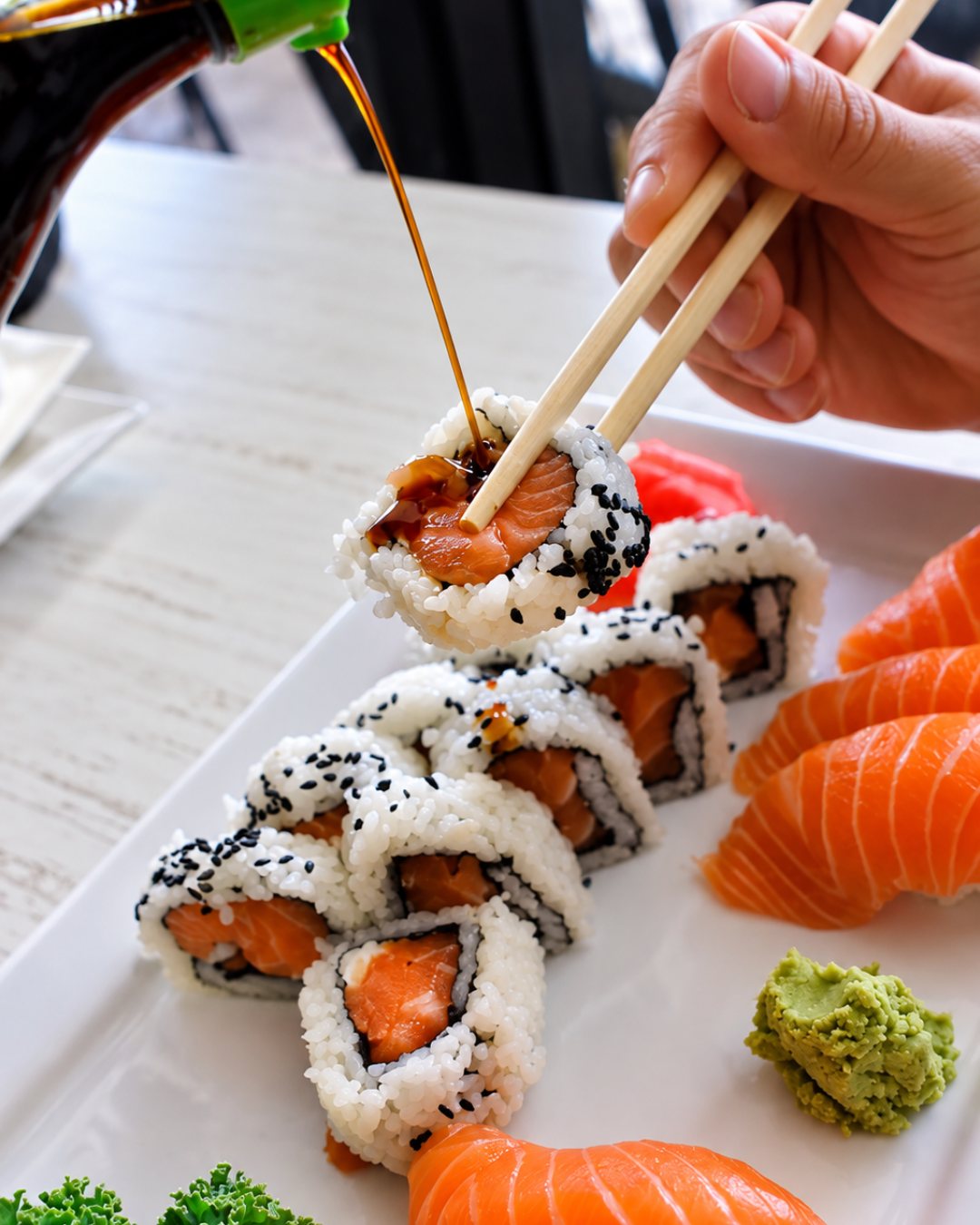 Soy sauce poured over a salmon roll held with chopsticks
