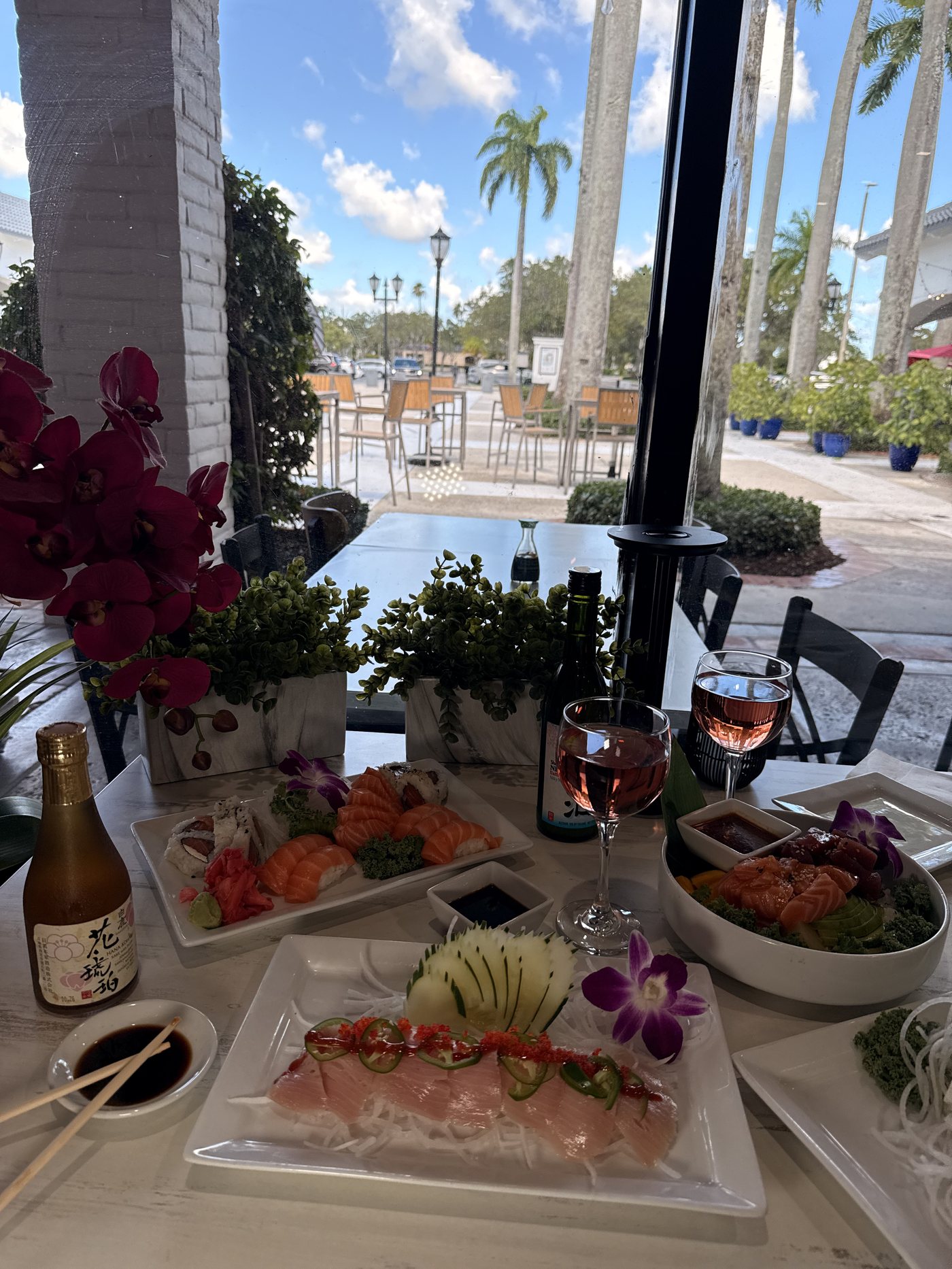 A bright window table at Sumo Sushi with a fresh sashimi platter, orchid and sake